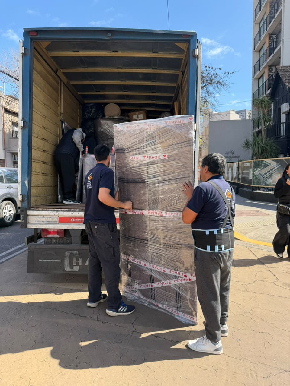 Integrantes del equipo acomodando un mueble alto envuelto en film dentro del camión