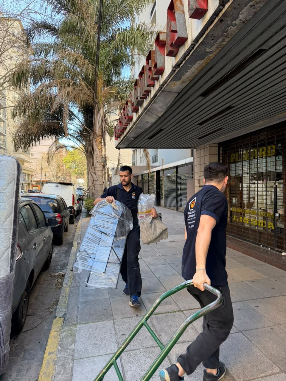 Dos integrantes del equipo llevando con carrito un mueble protegido con film por la vereda