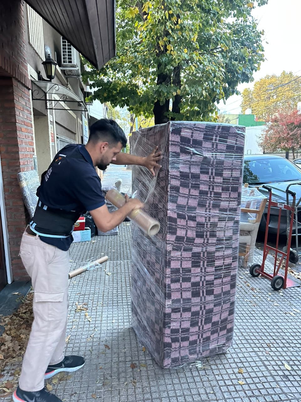 Integrante del equipo envolviendo con film un mueble protegido con mantas en la vereda