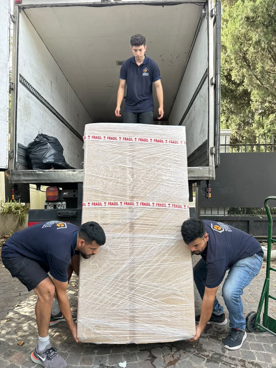 Integrantes del equipo bajando de un camión un mueble envuelto con film y cinta de frágil