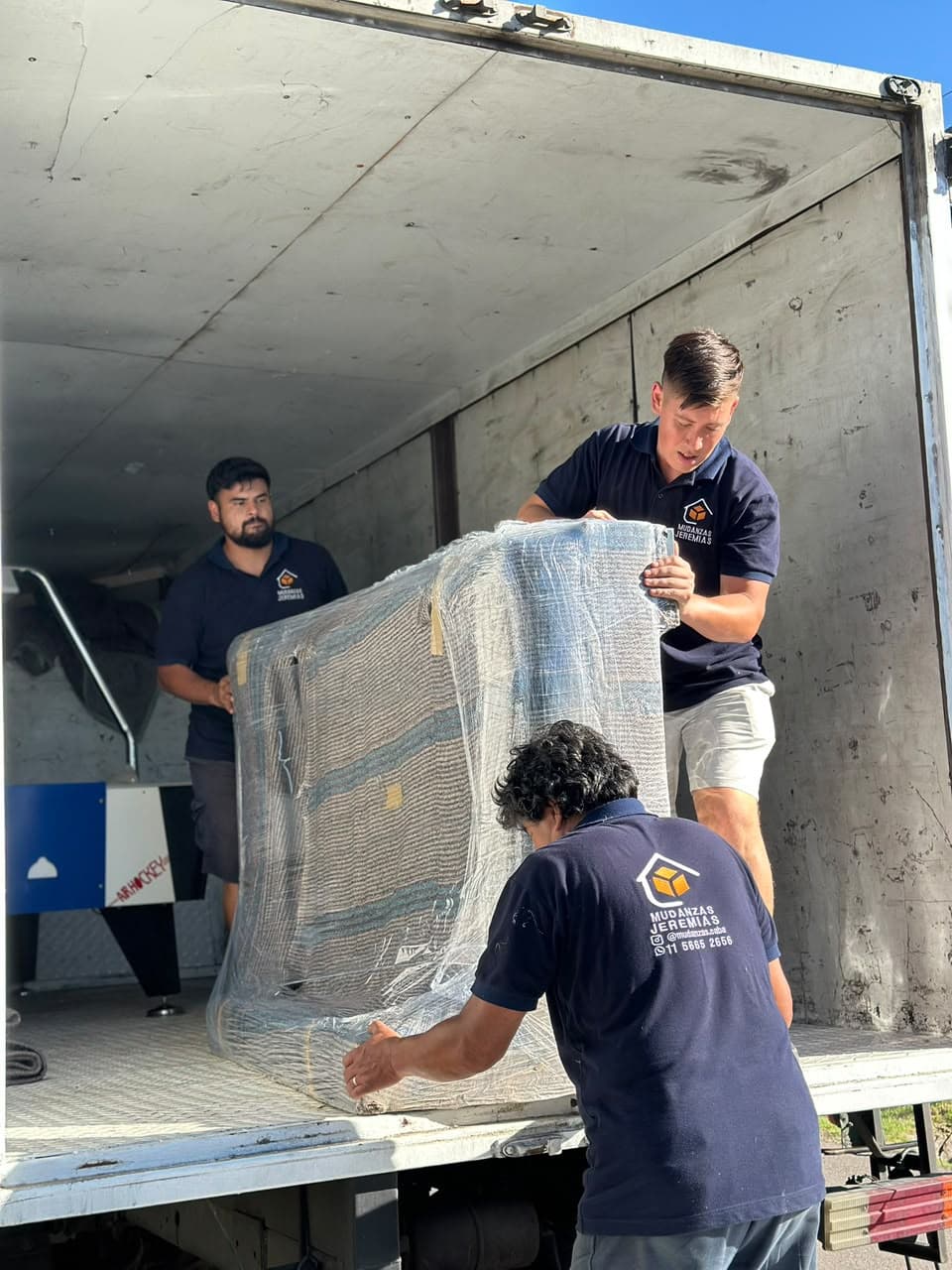 Tres integrantes del equipo moviendo un mueble envuelto dentro del camión