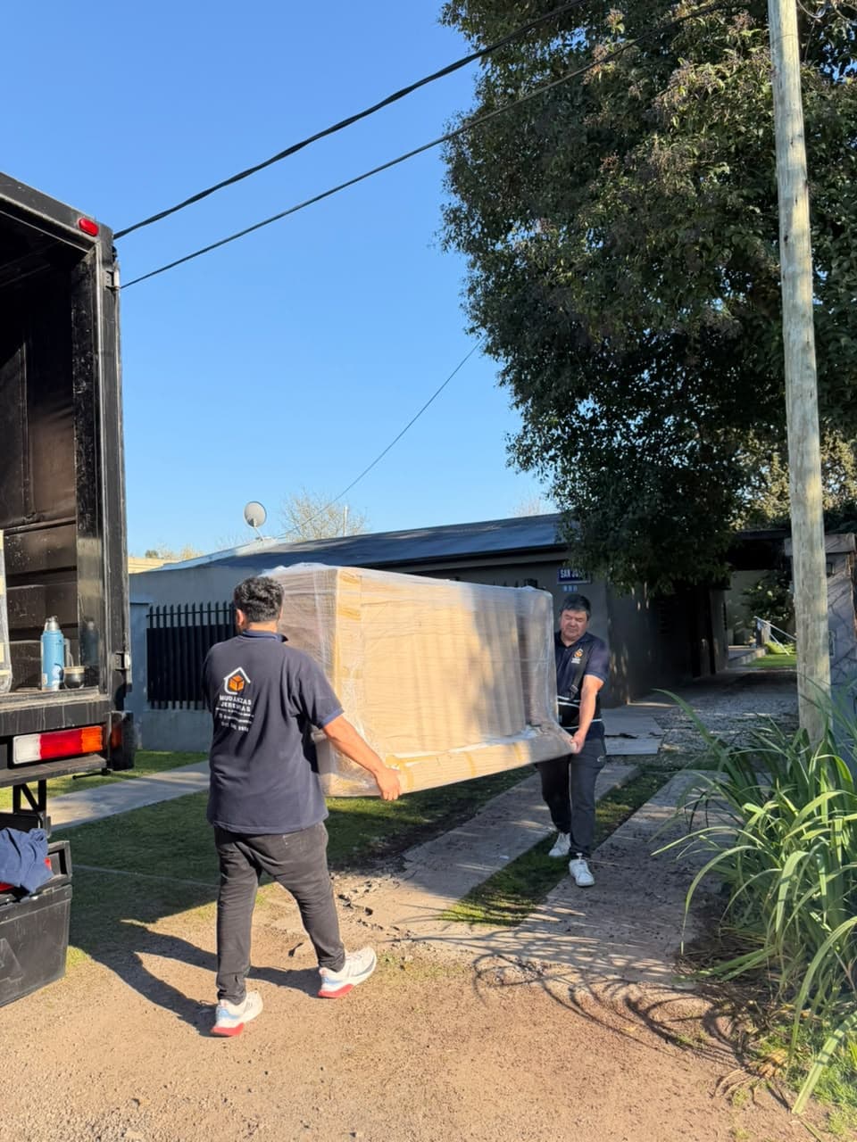 Integrante del equipo llevando un mueble envuelto en la vereda junto al camión